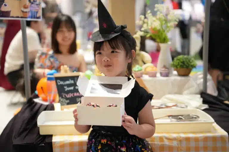 A young CEO in a witch hat showing her product at her booth